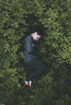 a man sitting in the middle of some bushes looking down at his face and hands