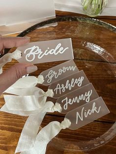 the bride and groom's name tags are being held by two hands on a wooden table