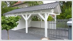 a white gazebo with a black roof and some bushes in front of the fence