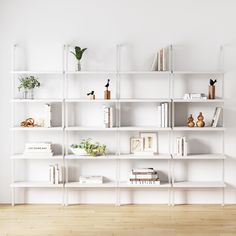 a white book shelf with books and plants on it in a room that has wood floors