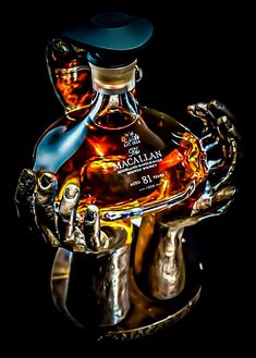 a bottle of macallan sitting on top of a metal holder with two hands holding it