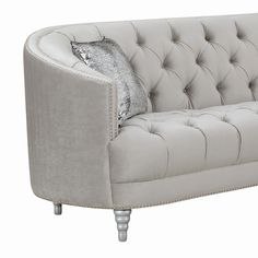 a white couch with silver pillows on the arm and backrests, sitting in front of a white background