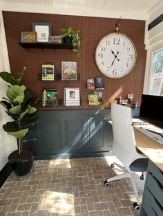 a room with a desk, chair and clock on the wall next to a potted plant