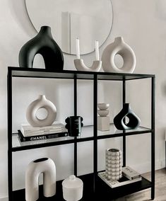 a shelf with vases and books on it in front of a wall mounted mirror