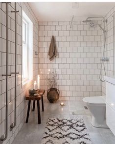 a white tiled bathroom with candles on the floor and a rug in front of it