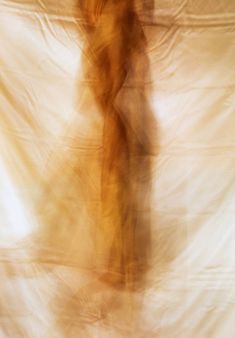 a blurry image of a woman standing in front of a white curtain with her hands behind her back