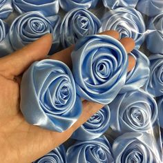 a hand is holding two blue roses in front of many other blue rose petals on display