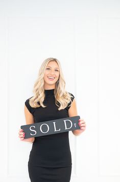 a woman holding up a sold sign in front of a white wall with the word sold written on it