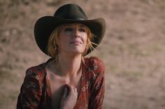 a woman wearing a hat standing in front of a dirt field with her hands on her chest