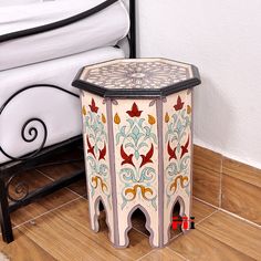 an ornately painted side table sits on the floor next to a bed with white sheets