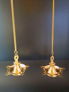 two gold - plated objects are hanging from chains on a black surface, one is empty and the other has a chain attached to it