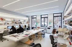 an office filled with people working on computers and desks in front of large windows