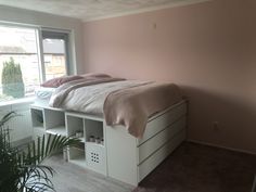 a bedroom with pink walls and white furniture in the foreground, there is a bed that has two drawers under it