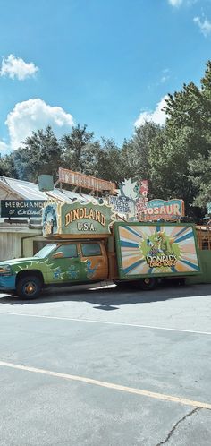 a green truck parked in front of a building with signs on it's side