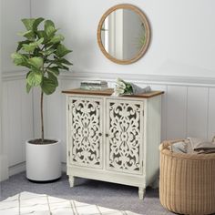 a white cabinet sitting next to a potted plant and a mirror on the wall