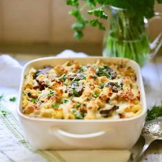 a casserole dish with mushrooms, cheese and parsley in front of a glass vase