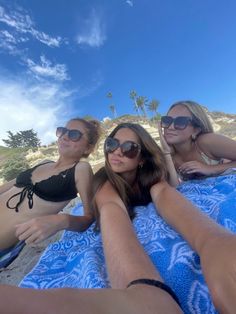 three beautiful women laying on top of a blue towel next to each other at the beach