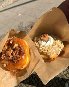 two donuts with toppings are in brown paper wrappers on the street side