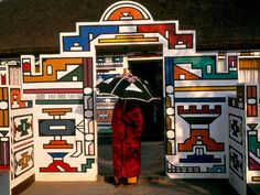 a woman with an umbrella stands in front of colorfully painted doors and doorways