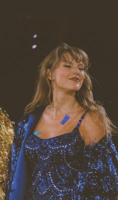 a woman in a blue dress standing on stage with her hands behind her back and eyes closed