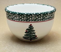 a white and green bowl with a christmas tree design on it's rim, sitting on a tan surface