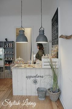 a woman standing behind a counter in a restaurant with hanging lights above it and food on the counter