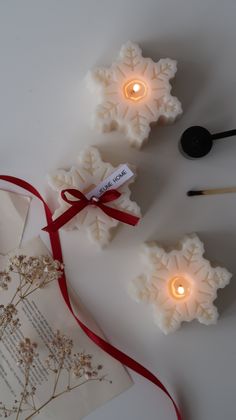 three snowflake candles are sitting next to an envelope with a red ribbon on it