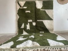 a large green and white rug on the floor next to a wall with a hat hanging above it