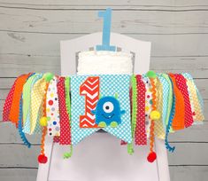 a birthday cake on top of a white chair with colorful ribbons around the neckline