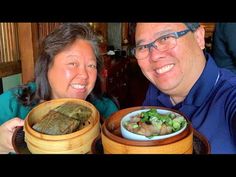 a man and woman sitting next to each other at a table with food in bowls