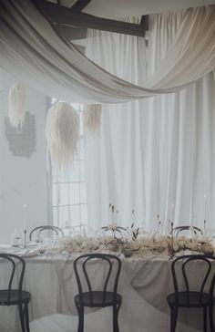 the table is set with white linens and black chairs, along with tall centerpieces