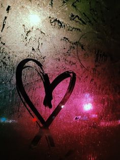 a heart drawn in the frosted glass on a rainy window with lights behind it