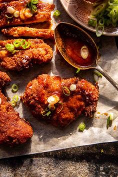 fried chicken with sauce and green onions on a sheet of paper next to a spoon