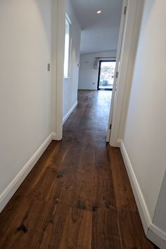 an empty hallway with hard wood flooring and white walls, leading to the front door