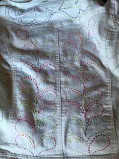 the back of a white jacket with colorful stitching on it's sleeves and bottom