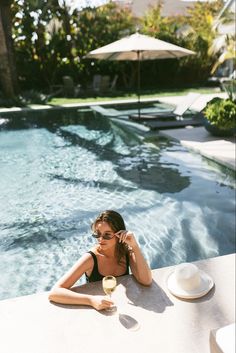 a woman sitting at the edge of a pool with a glass of wine in her hand