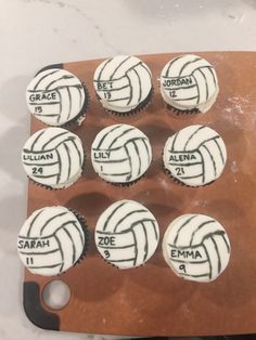 cupcakes with white and black icing on a wooden tray that says volleyball