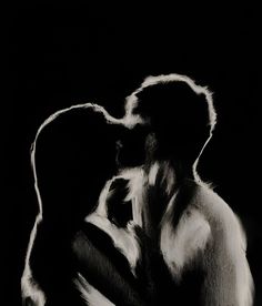 a black and white photo of a man kissing a woman's head in front of a dark background