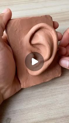 two hands are holding clay that is shaped like an ear and has a video playing on it