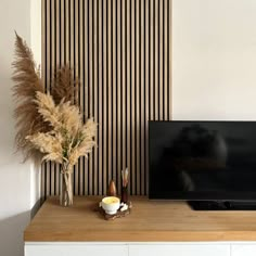 a flat screen tv sitting on top of a wooden table next to a vase filled with flowers