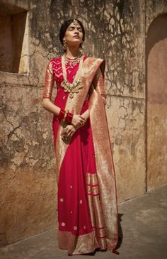 a woman wearing a red and gold sari standing in front of a stone wall