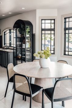 a dining room table with chairs and a vase filled with flowers on top of it