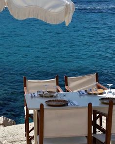 an umbrella is hanging over a table set for two by the water's edge