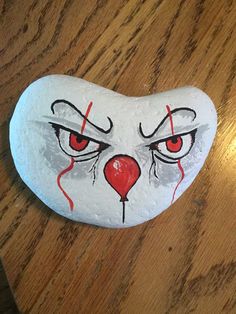 a painted rock that looks like a scary clown's face on a wooden table