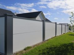 a white fence in front of a house with green grass and trees on the other side