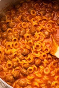 a pot filled with pasta and meatballs on top of a counter next to a wooden spoon