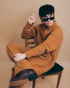 a man sitting on top of a wooden chair wearing sunglasses and pointing to the side