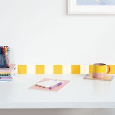 a white desk topped with a yellow and pink mug next to a stack of books