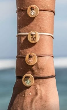 a person's arm with four different bracelets on it and the ocean in the background