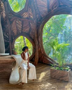 a woman sitting on a bench in front of a tree trunk structure with large round windows